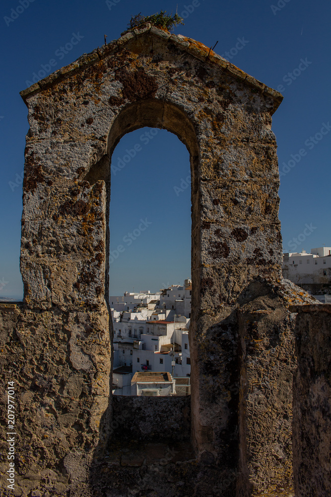 Ancient stone arch of the medieval era. View of a small white Spanish village.