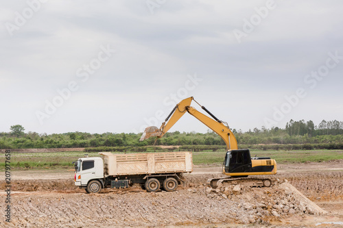 Yellow excavator machine loading soil into a dump truck at construction site
