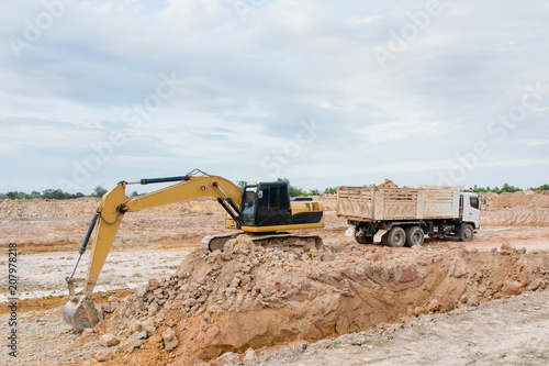 Yellow excavator machine loading soil into a dump truck at construction site