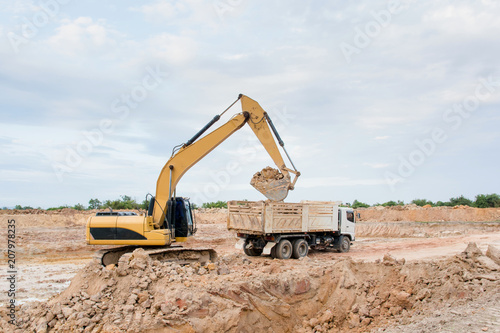 Yellow excavator machine loading soil into a dump truck at construction site