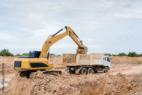 Yellow excavator machine loading soil into a dump truck at construction site
