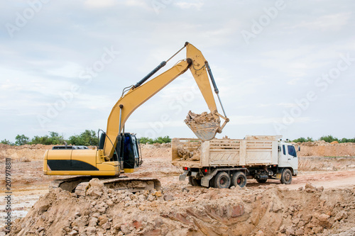 Yellow excavator machine loading soil into a dump truck at construction site