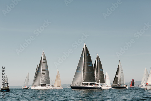 sailboats with dark sails lining up for yacht race to begin