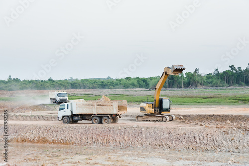 Yellow excavator machine loading soil into a dump truck at construction site