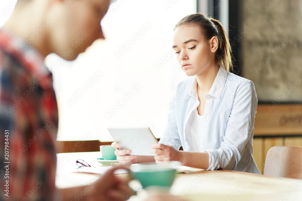 Casual teen girl watching tablet sitting at table with coffee and anonymous students Casual teen girl watching tablet sitting at table with coffee and anonymous students