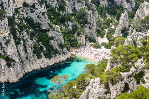 View from above of the calanque of En-Vau, a hard-to-reach narrow natural creek with white sandy beach close to Marseille and Cassis, with people sunbathing and swimming in the crystal clear water. © olrat