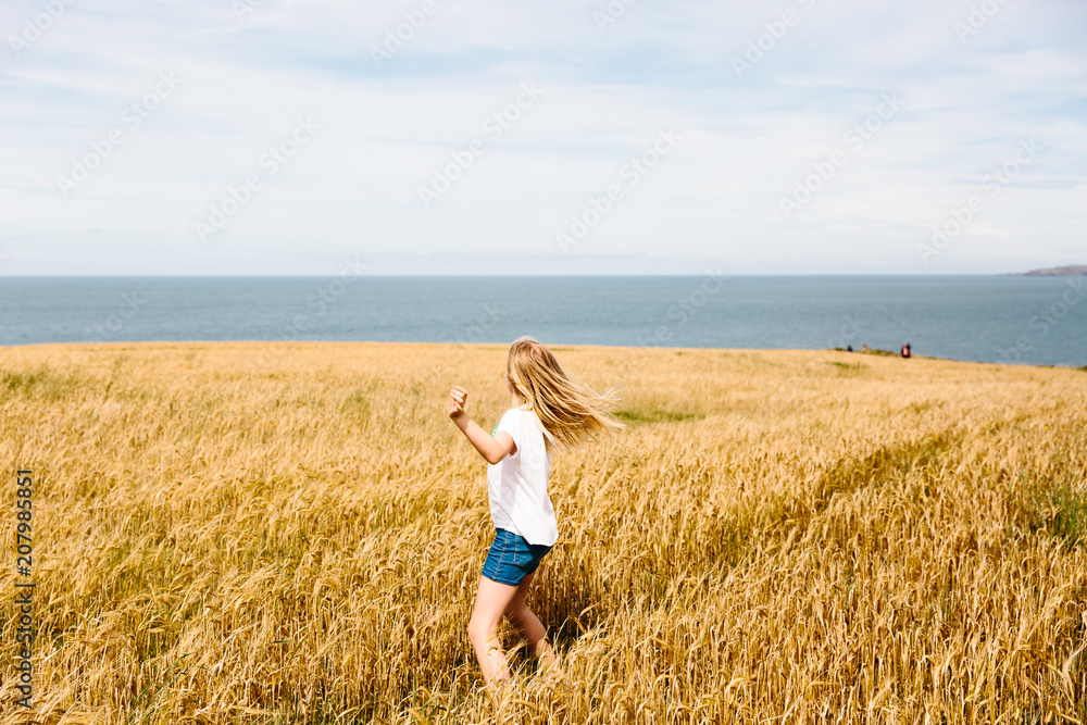 Little girl running through a field of ripe wheat with the sea in the background Little girl running through a field of ripe wheat with the sea in the background