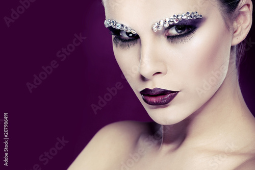 Portrait of sexual beautiful girl with strasses on face, on a violet background