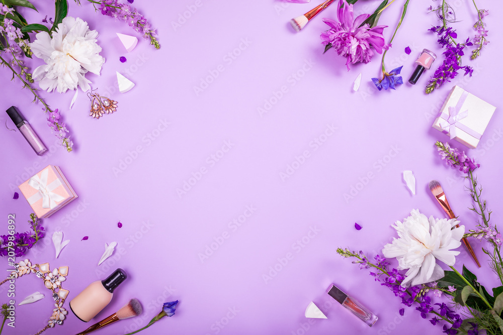 Set of cosmetics, brushes and jewellery with fresh flowers on purple background. Summer sale. Shopping