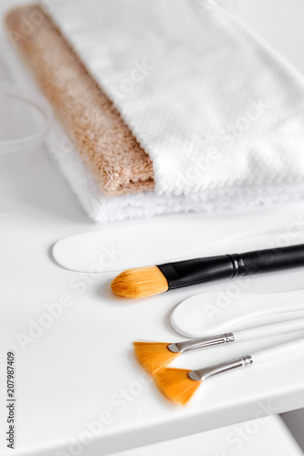 Cosmetic nylon brushes, plastic spatulas and a stack of folded towels on the surface of the white shelf. Various accessories for different procedures for skin care for face and body. Cosmetology