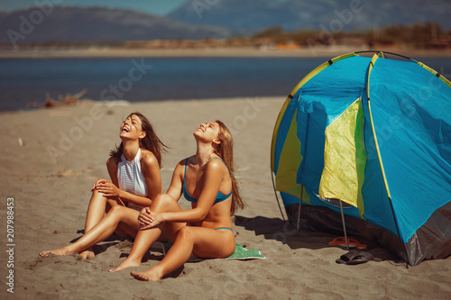 Two young happy woman camping on the beach during the summer