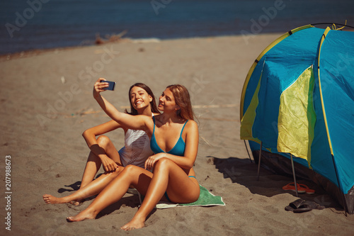 Two young happy woman camping on the beach during the summer