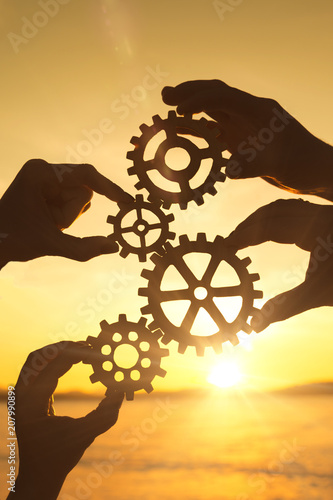 Four businessmen's hands collect a puzzle of gears against the sunset. Business concept idea, strategy cooperation teamwork, creative