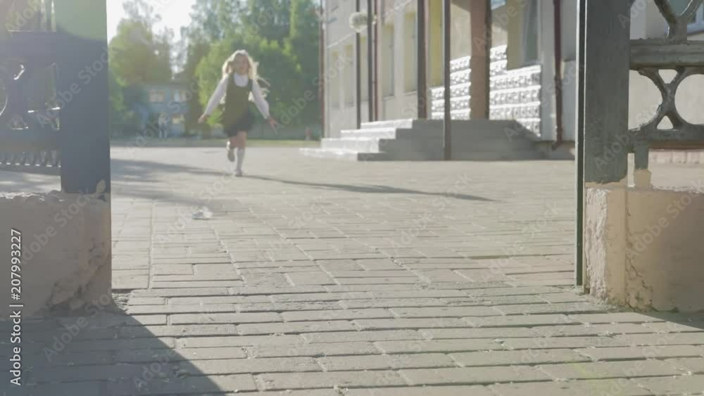 A little funny schoolgirl in school uniform and a briefcase on her shoulders runs out of school. Steadicam shot A little funny schoolgirl in school uniform and a briefcase on her shoulders runs out of school. Steadicam shot