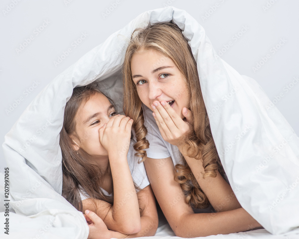 Sisters sharing a secret whispering under the quilt Sisters sharing a secret whispering under the quilt