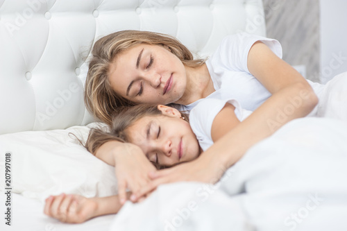 Mom and daughter sleep together on the bed in the bedroom