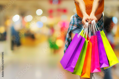 Smiling beautiful young woman holding many colorful shopping bags over Shopping malls background. happiness, consumerism, sale and people concept.