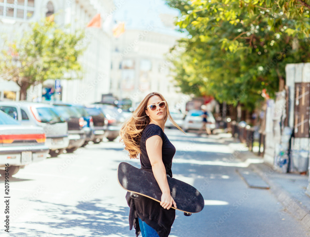 A woman with a skateboard and wearing sunglasses on a sunny day