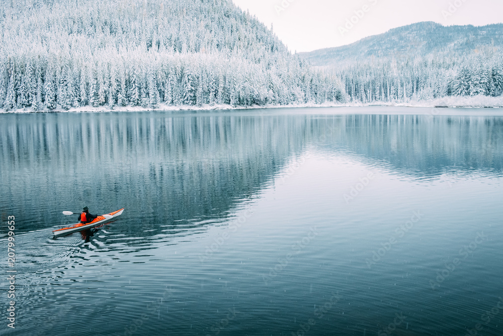 A solo kayaker paddles on a still lake one quiet winter morning in Montana A solo kayaker paddles on a still lake one quiet winter morning in Montana