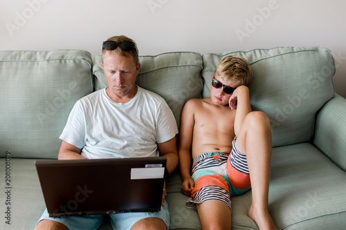 father working while on vacation; his bored son waits for him to finish photo