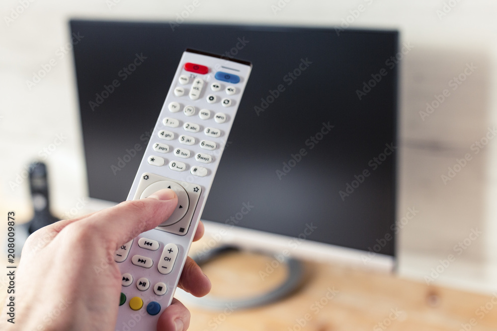 TV Remote Control in Hand with Flat-Screen TV in Background TV Remote Control in Hand with Flat-Screen TV in Background
