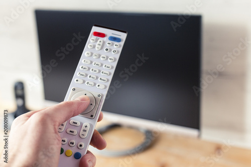 TV Remote Control in Hand with Flat-Screen TV in Background