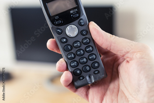 Cordless Telephone in Hand with Computer Monitor in Background