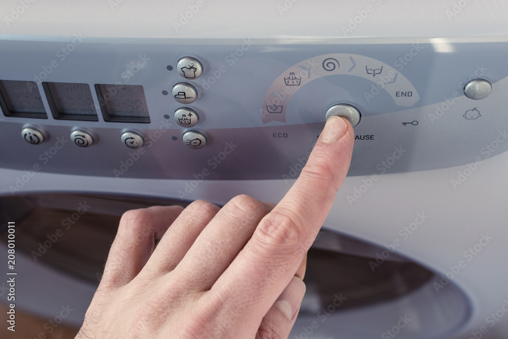 Finger Pushing Start/Pause Button on Washing Machine Dashboard Stock