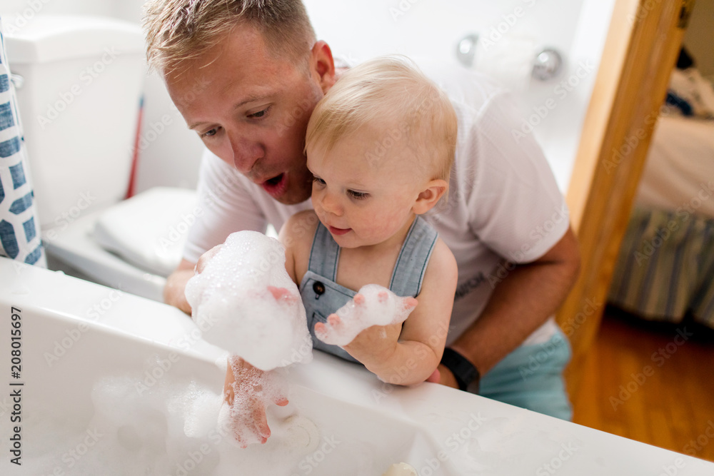 father and toddler son blowing bubbles into the tub before a bath father and toddler son blowing bubbles into the tub before a bath