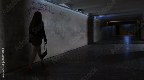 Drunk boozy female in mini skirt and high heeled shoes walking alone in dark underpass tunnel alone. Tipsy woman stumbling and touching the wall trying to find the way home at night