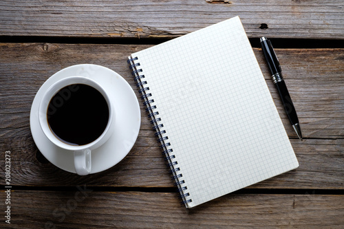 Notebook, pen and a cup of coffee on wooden table. 