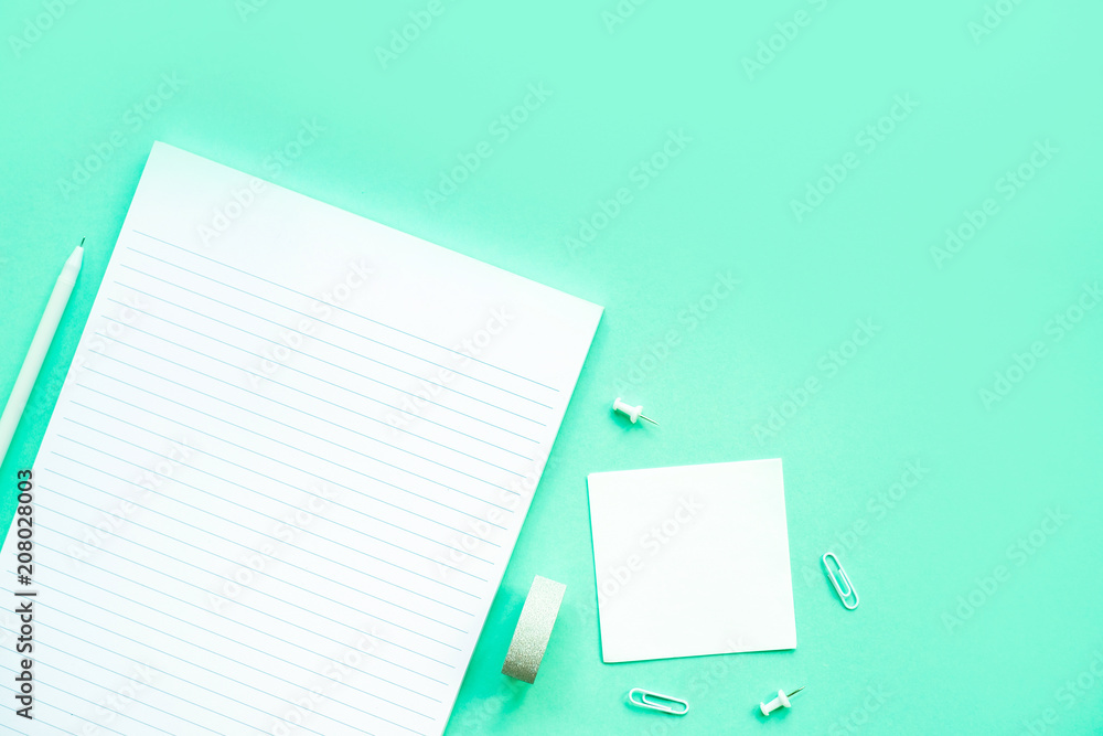 Beautiful office stationery flatlay with ruled notebook, pen, sticky note and paper clip on the bright desk with turquoise background. Beautiful office stationery flatlay with ruled notebook, pen, sticky note and paper clip on the bright desk with turquoise background.