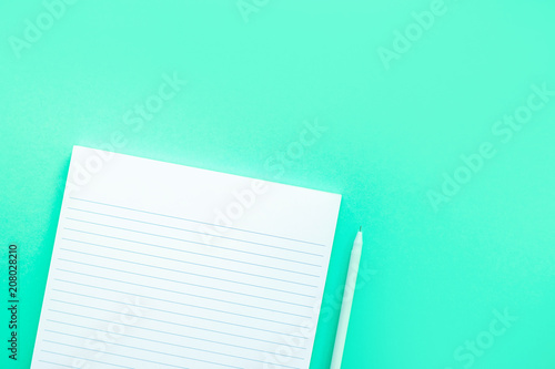 Beautiful office stationery flatlay with ruled notebook and white pen on the bright desk with turquoise background.