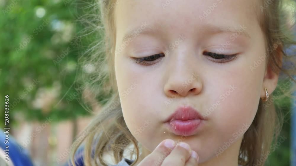 Little kid girl closeup face portrait eating ripe strawberry during walking in park Little kid girl closeup face portrait eating ripe strawberry during walking in park