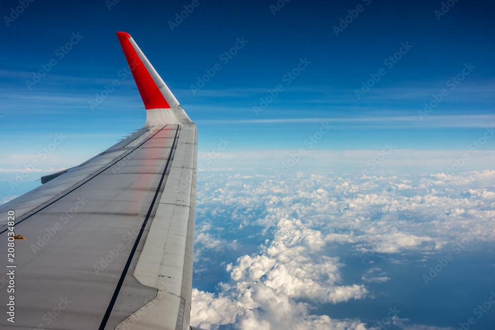 Wing of an airplane flying above the clouds. Wing of the plane on blue sky background., Traveling concept.Wing of an airplane flying above the clouds. Wing of the plane on blue sky background.