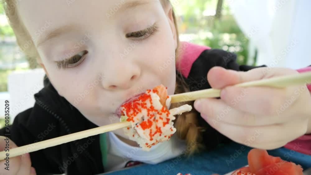 Cute little kid girl in restaurant funny try eating sushi with chinese chopsticks in slow motion Cute little kid girl in restaurant funny try eating sushi with chinese chopsticks in slow motion