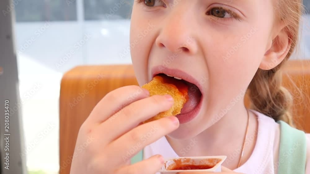 Cute little kid girl face portrait eating chicken nuggets with ketchup in fast food restaurant Cute little kid girl face portrait eating chicken nuggets with ketchup in fast food restaurant