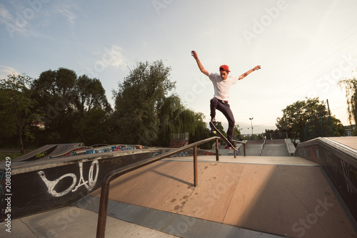 Skateboarder performing extreme tricks on narrow railing in skate park photo