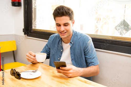 young student using his smart phone to read text while having a coffee