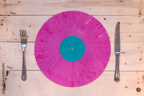 Pink vinyl record in the form of a plate with fork and knife on a wooden table background. Music has definitely good taste.
