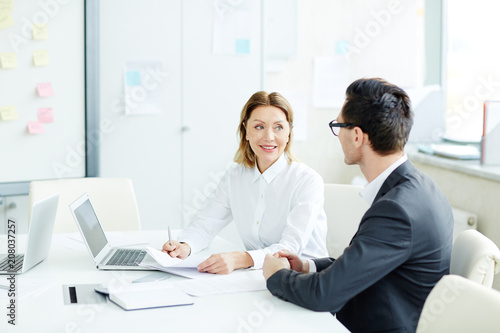 Female and male office workers sitting at desk in office room on business meeting looking at each other 