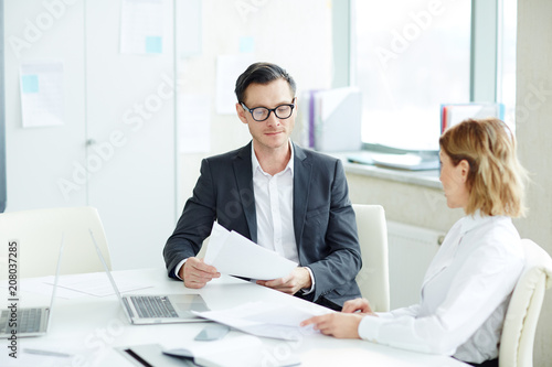 Man and woman in official clothes sitting at desk in tidy office reading documentation