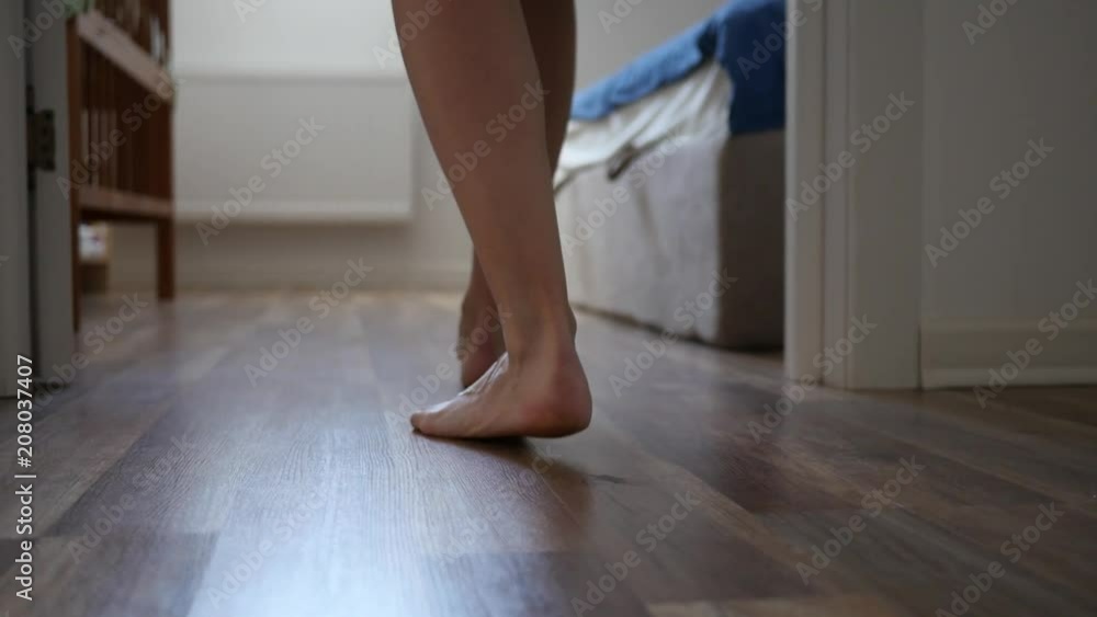 Barefoot woman walks into a room stepping onto a laminate legs camera slow motion