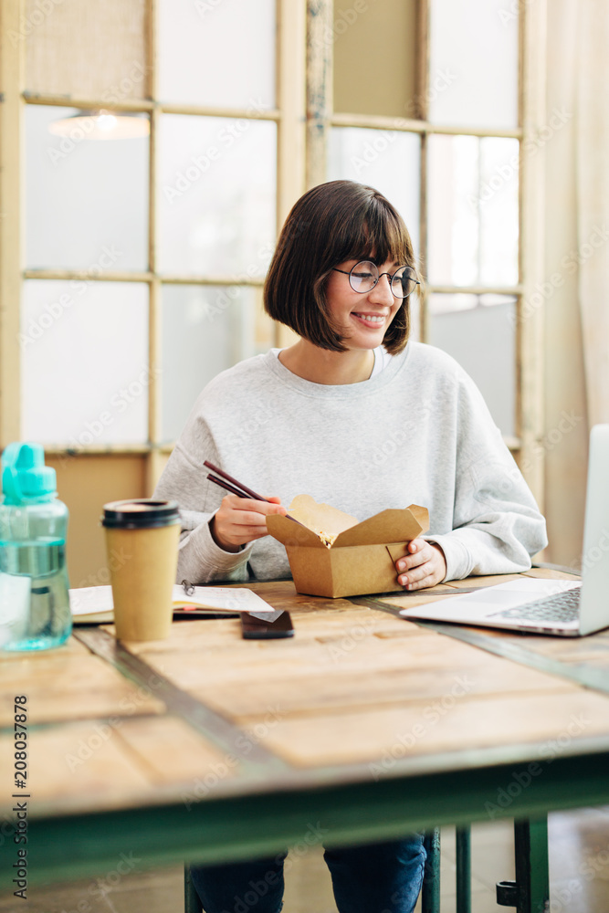 Woman working with laptop while having a lunch in a co-working office. Woman working with laptop while having a lunch in a co-working office.