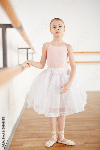 Girl in tutu and pointe having lesson in dancing school and looking at camera