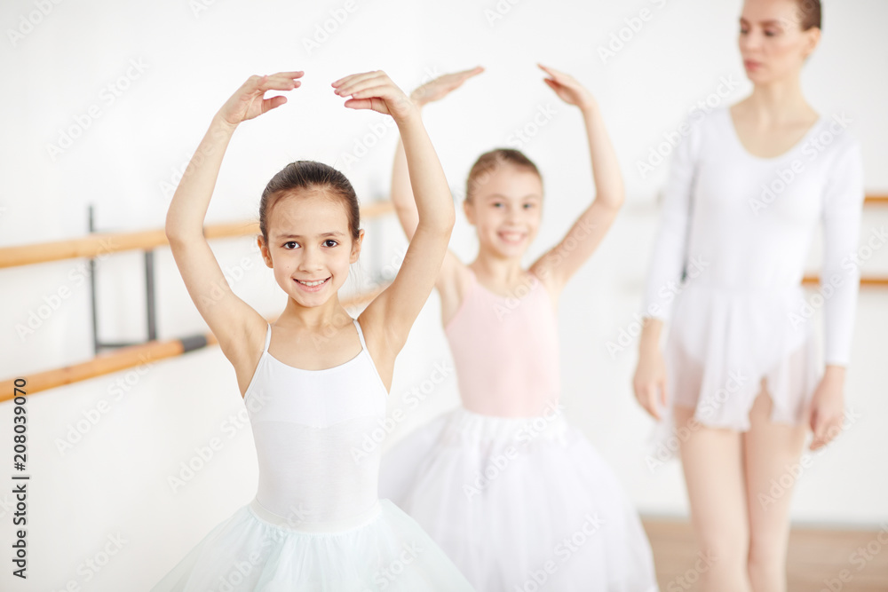 Pretty young ballerinas smiling and staying in pose in white room with adult teacher Pretty young ballerinas smiling and staying in pose in white room with adult teacher