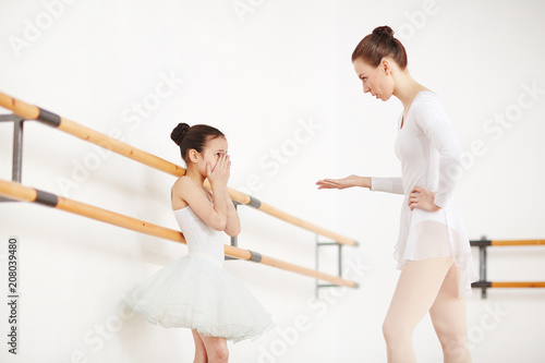 Ballerinas in white clothes and tutu staying in dancing studio at wooden machine and discussing 