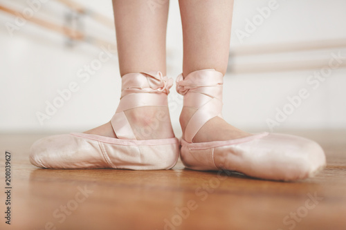 Small girls feet in light ballet shoes champagne color staying in pose on floor in studio