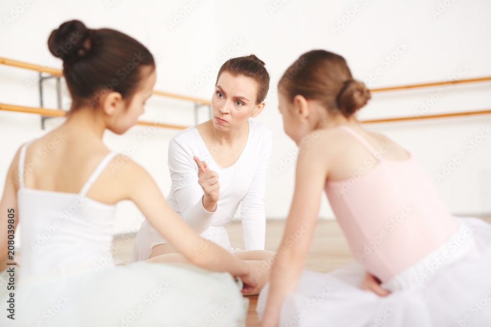 Fototapeta premium Little ballerinas in white clothes sitting back and listening pedagogue in ballet studio 