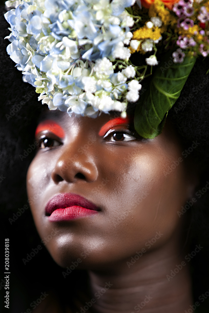 	 black woman with Afro and flowers is happy. she's wearing red lipstick and nice foundation. she has a bright smile on her face and she models in the studio